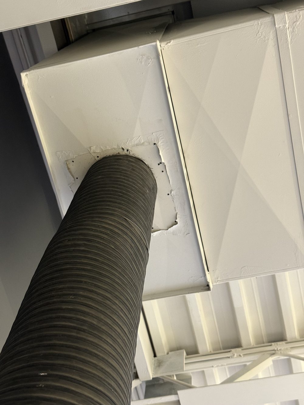 A large negative-air vacuum hose sealed into a cut opening in the main trunk line of a basement duct system, taped airtight so the whole system can be put under negative pressure.